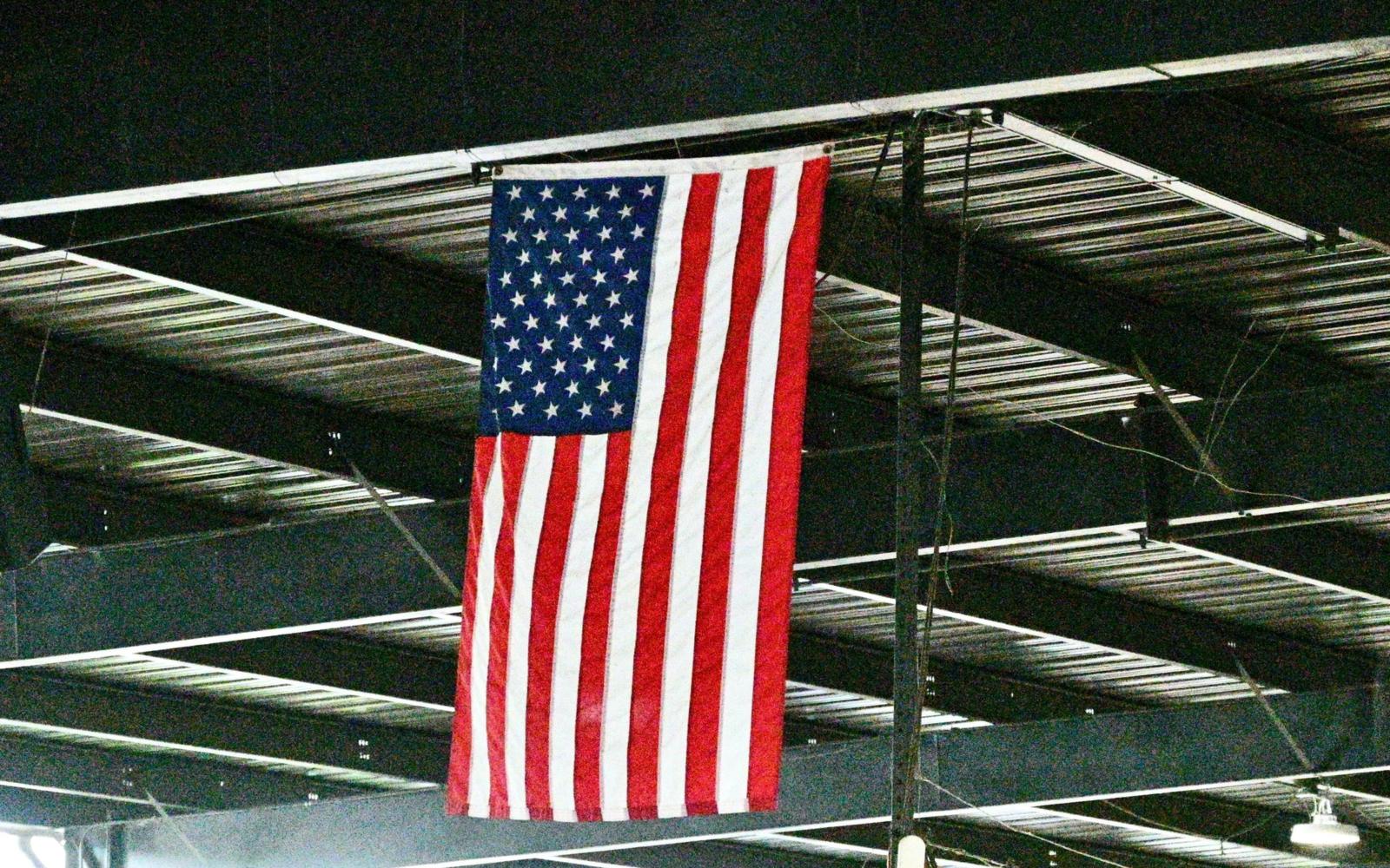 An American flag hanging from the steel rafters of a hangar